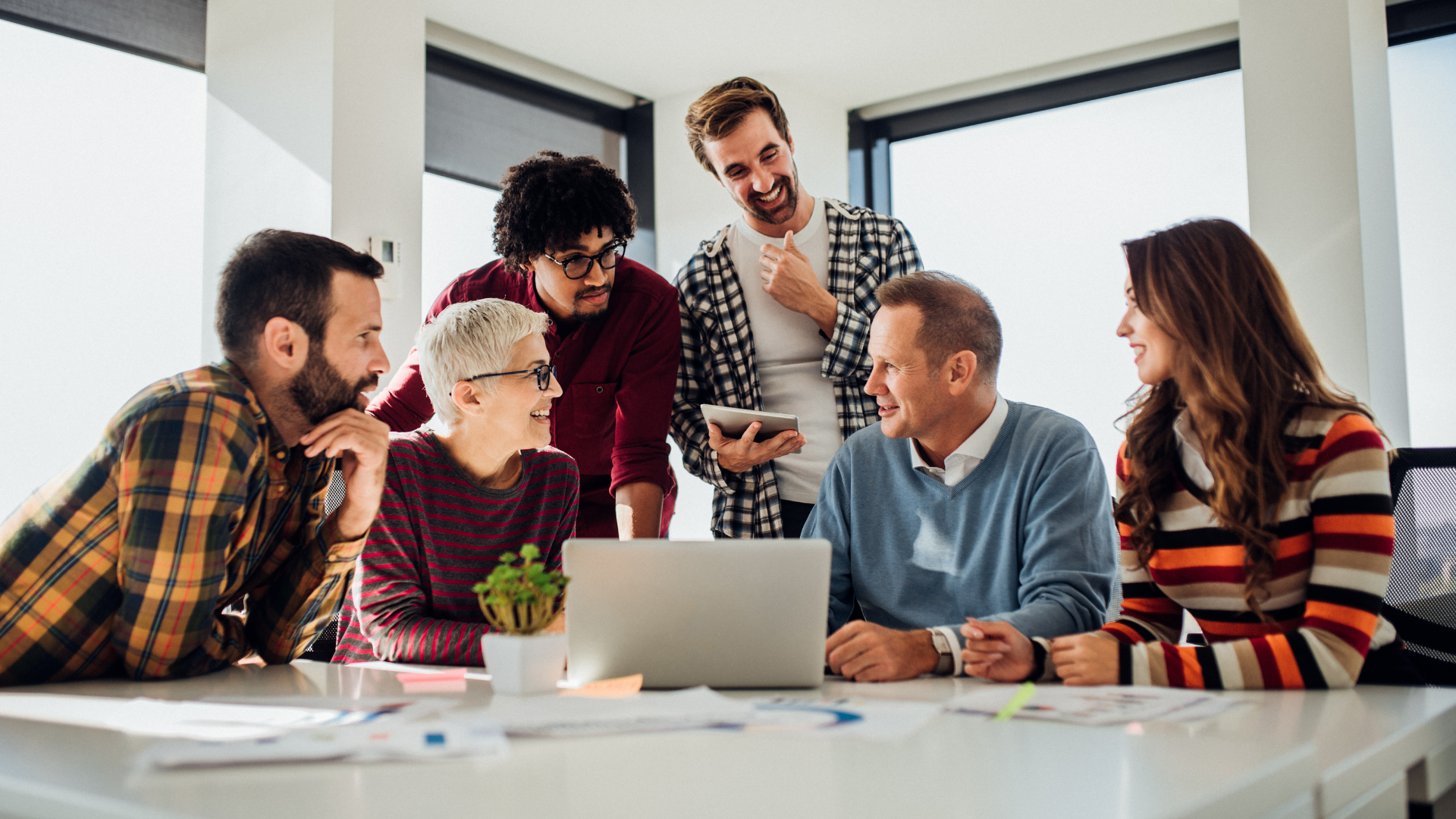 A group of colleagues of varied backgrounds gathered around a laptop, reviewing a job description in a modern office. The image conveys teamwork, collaboration, and strategic discussion—ideal for highlighting a legal hiring process.