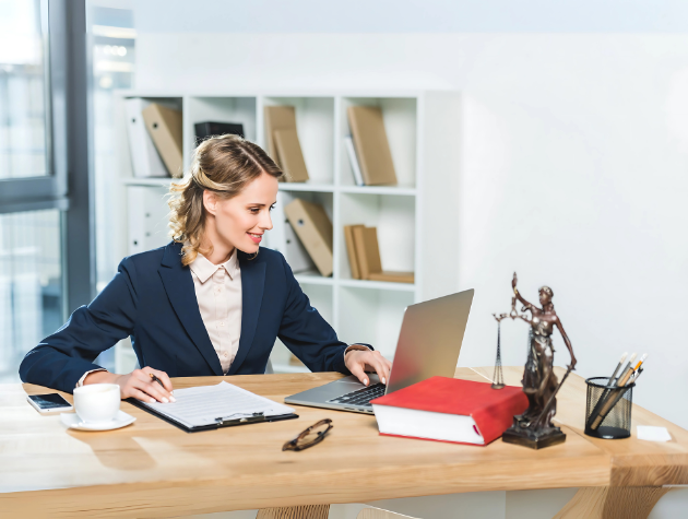 Female lawyer working on laptop with legal documents and Lady Justice statue on desk