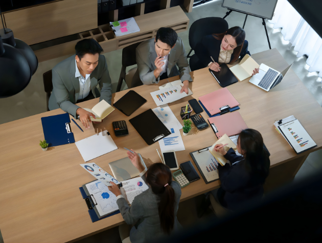 Team of professionals in a workplace meeting reviewing documents, charts, and laptops, symbolizing collaboration to embed privacy as product safety in product development.